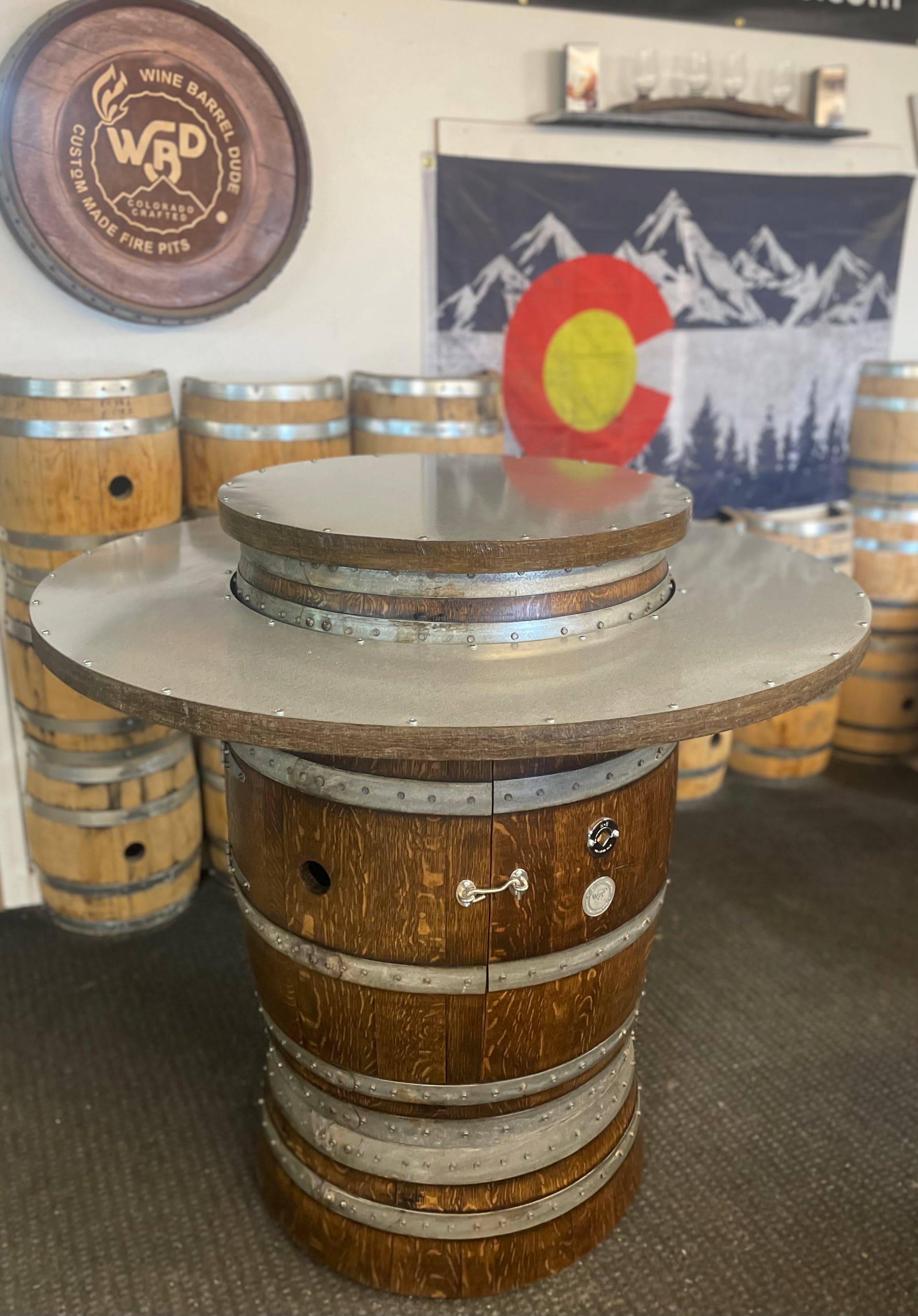 A finished barrel table in the Wine Barrel Dude showroom, with the Colorado flag and the barrel-lid sign behind it