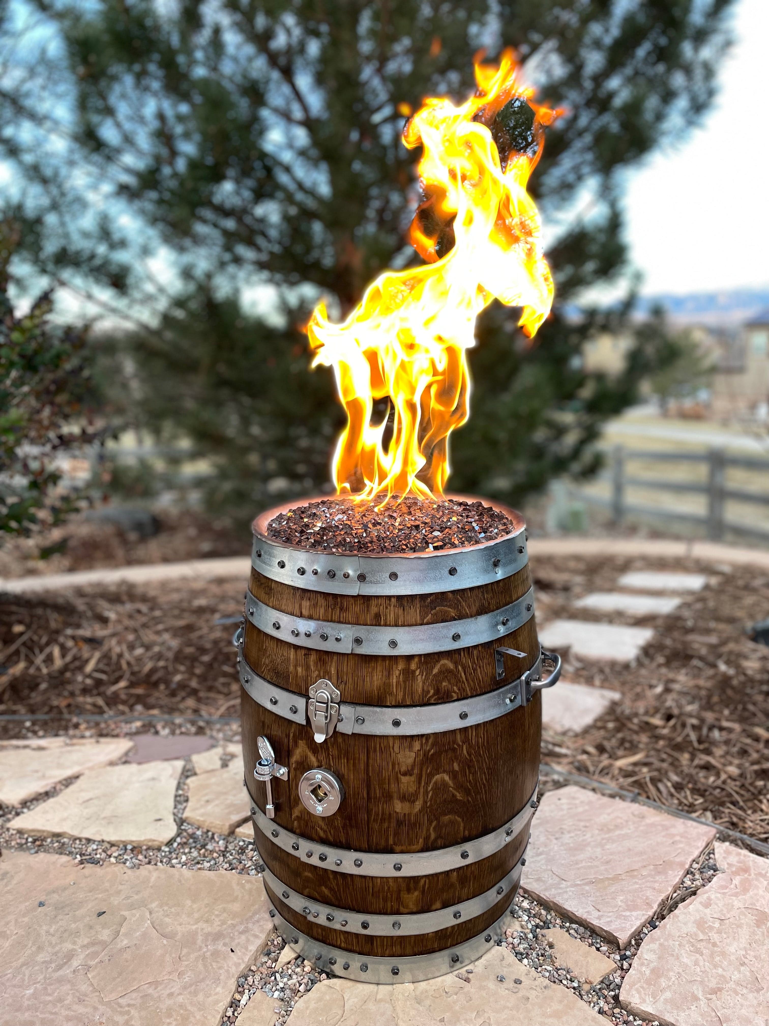 Upright oak barrel fire pit with a tall flame on a flagstone patio, pine trees behind