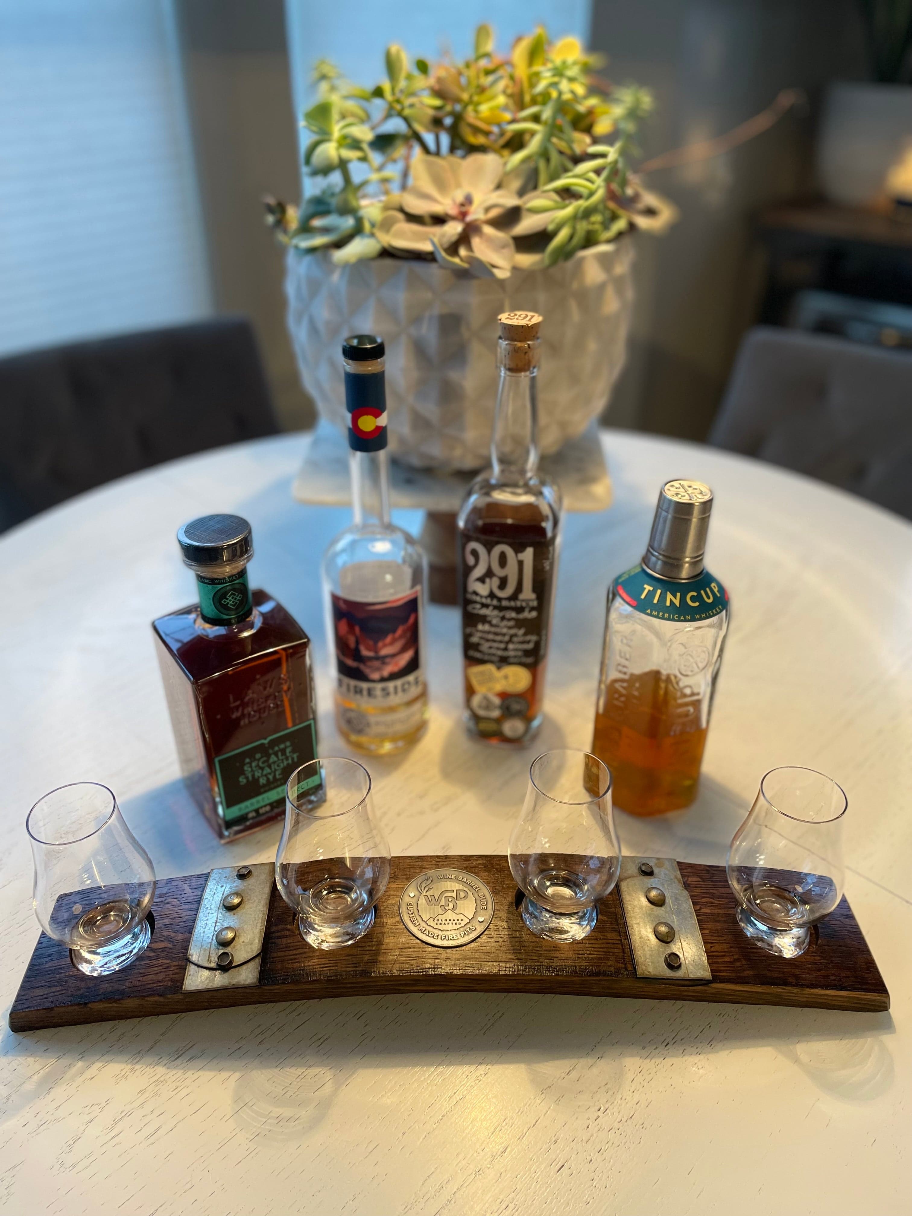 Barrel stave flight board holding four whiskey glasses beside whiskey bottles