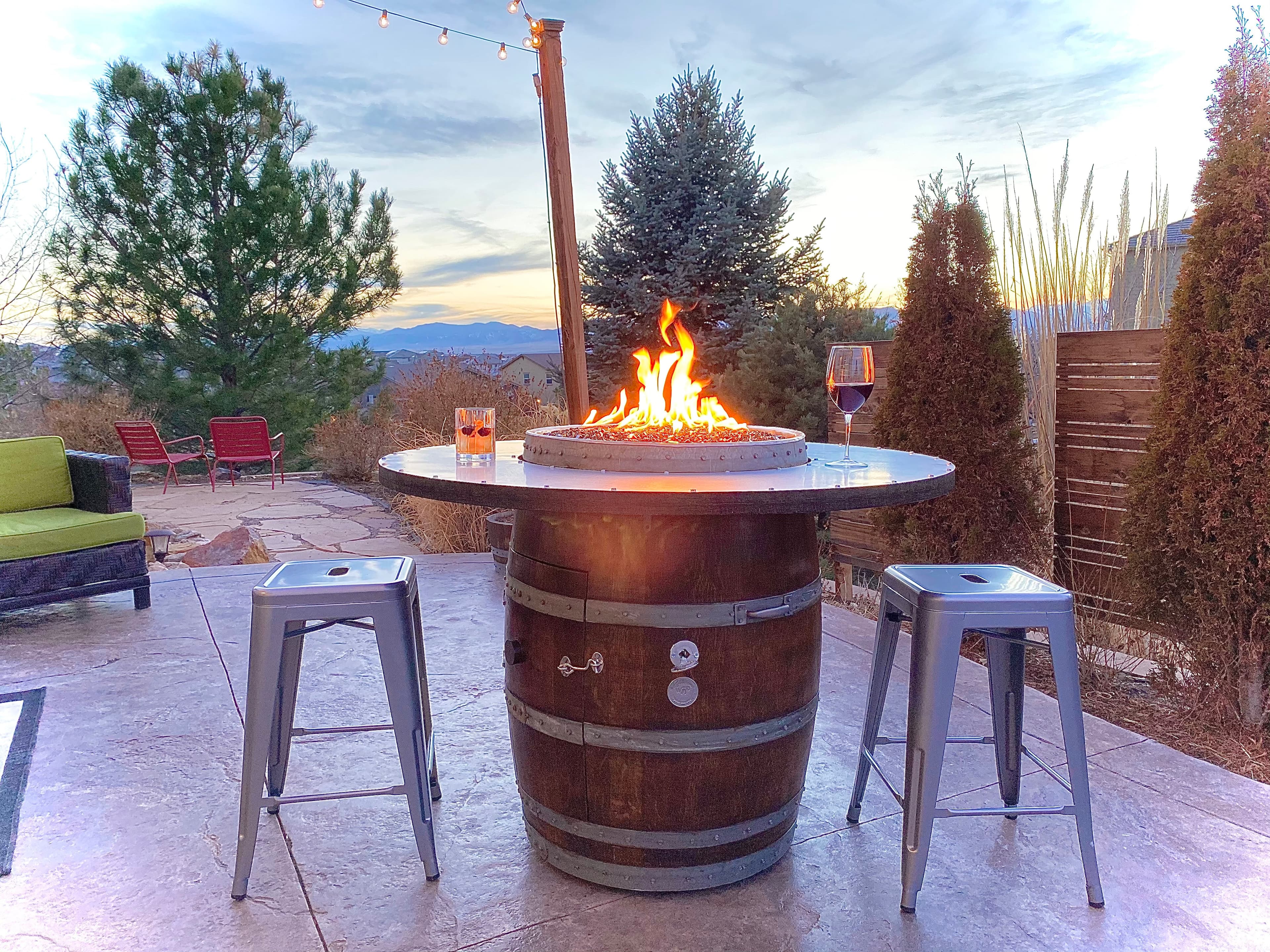Tall wine barrel fire pit table with two metal stools on a patio at dusk